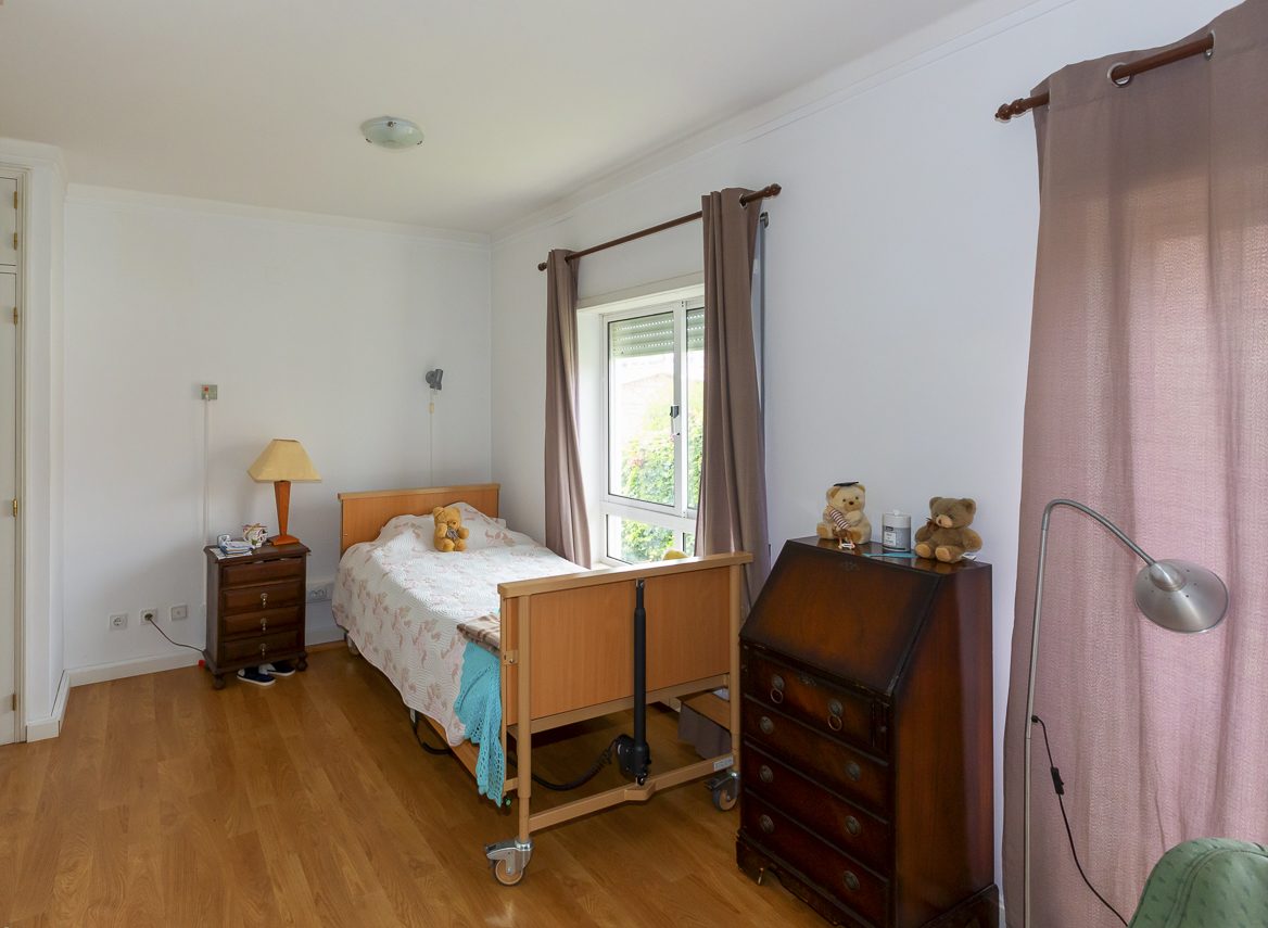 A bedroom with personal furniture, a lamp and a garden-facing window
